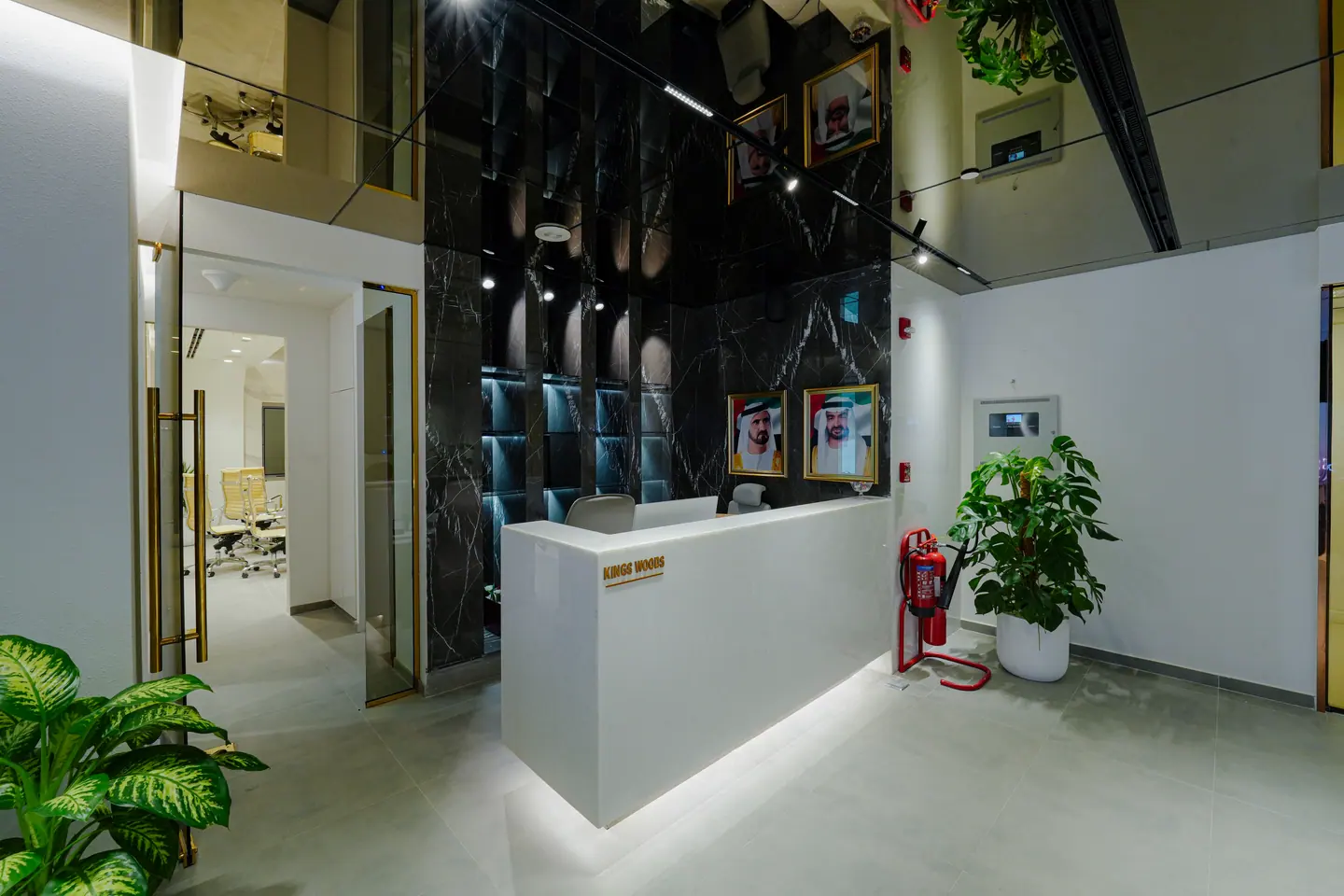 Freestanding reception desk against a book-matched dark marble wall, with planting and a glazed partition to the office floor — Kings Woods Real Estate office fit-out by Urban Crown, Dubai