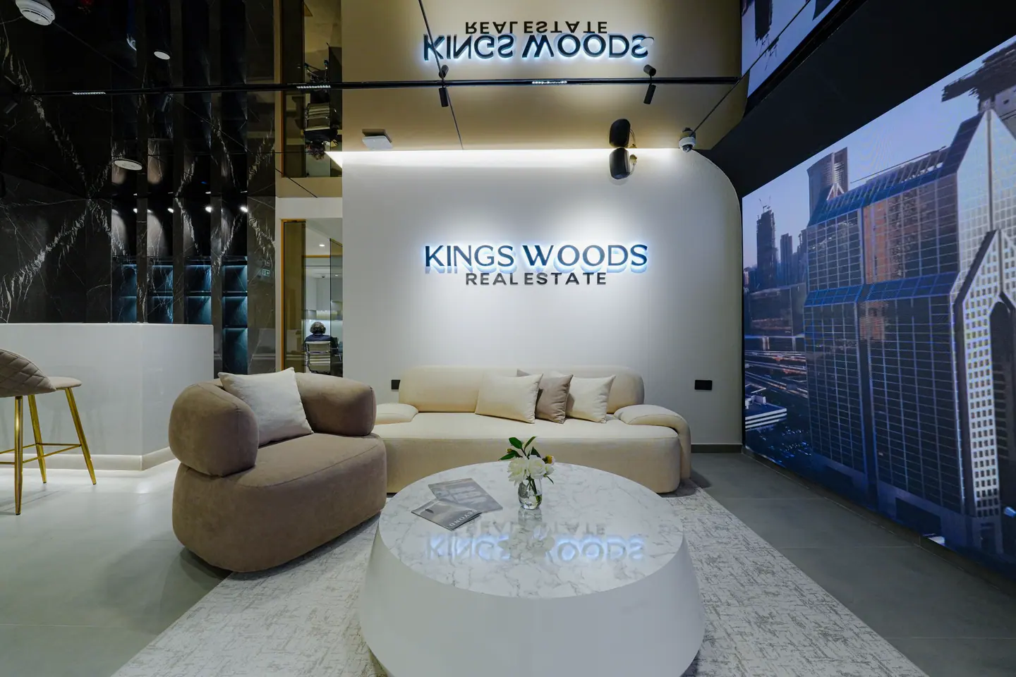 Lounge and meeting nook with a channel-lit Kings Woods Real Estate sign, curved seating and a round coffee table — Kings Woods Real Estate office fit-out by Urban Crown, Dubai