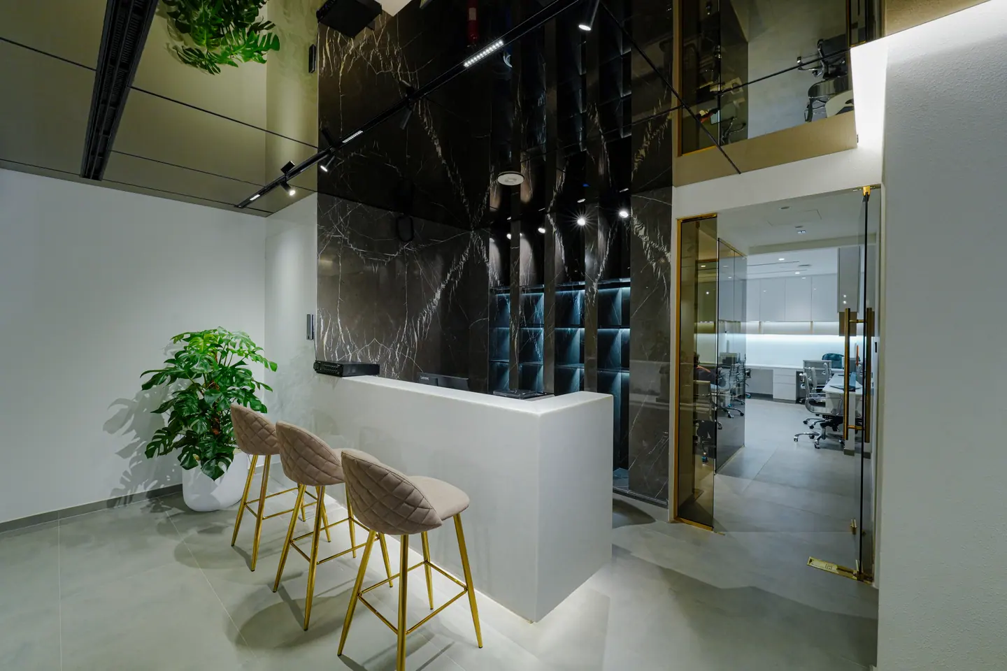 Dark stone breakout bar counter with stools and a glazed partition between the open office and private rooms — Kings Woods Real Estate office fit-out by Urban Crown, Dubai