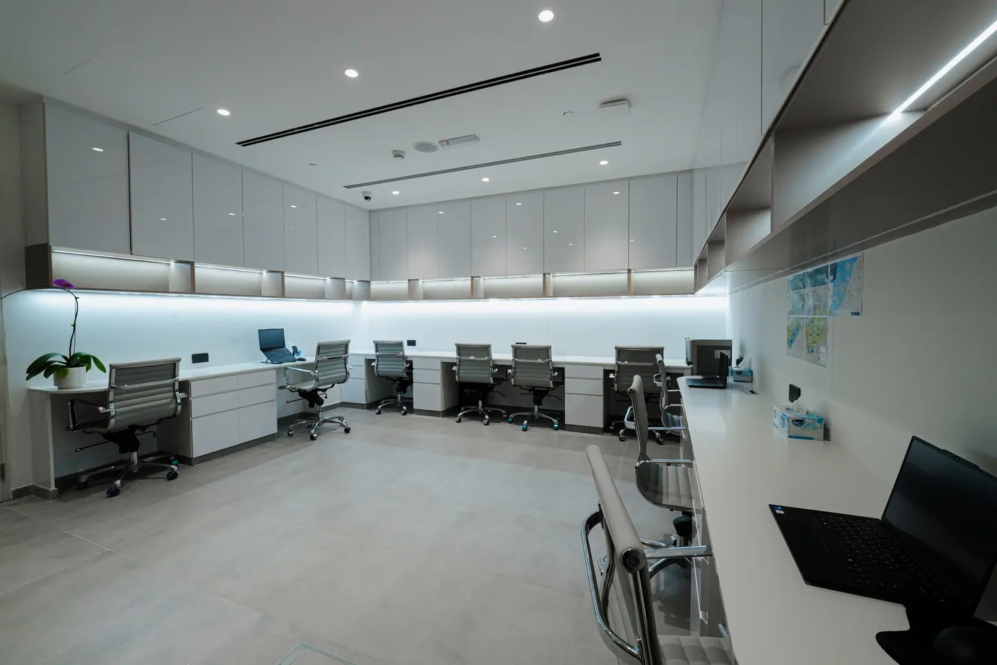 Row of open-plan workstations beneath continuous overhead cabinetry with backlit underside lighting — Kings Woods Real Estate office fit-out by Urban Crown, Dubai